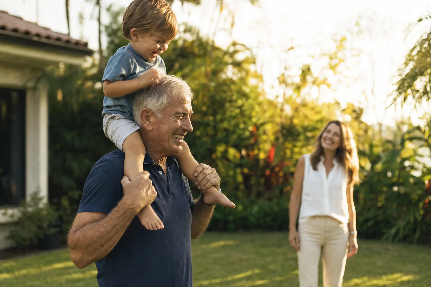 A grandfather lifting a small child onto his shoulders in a sunlit garden